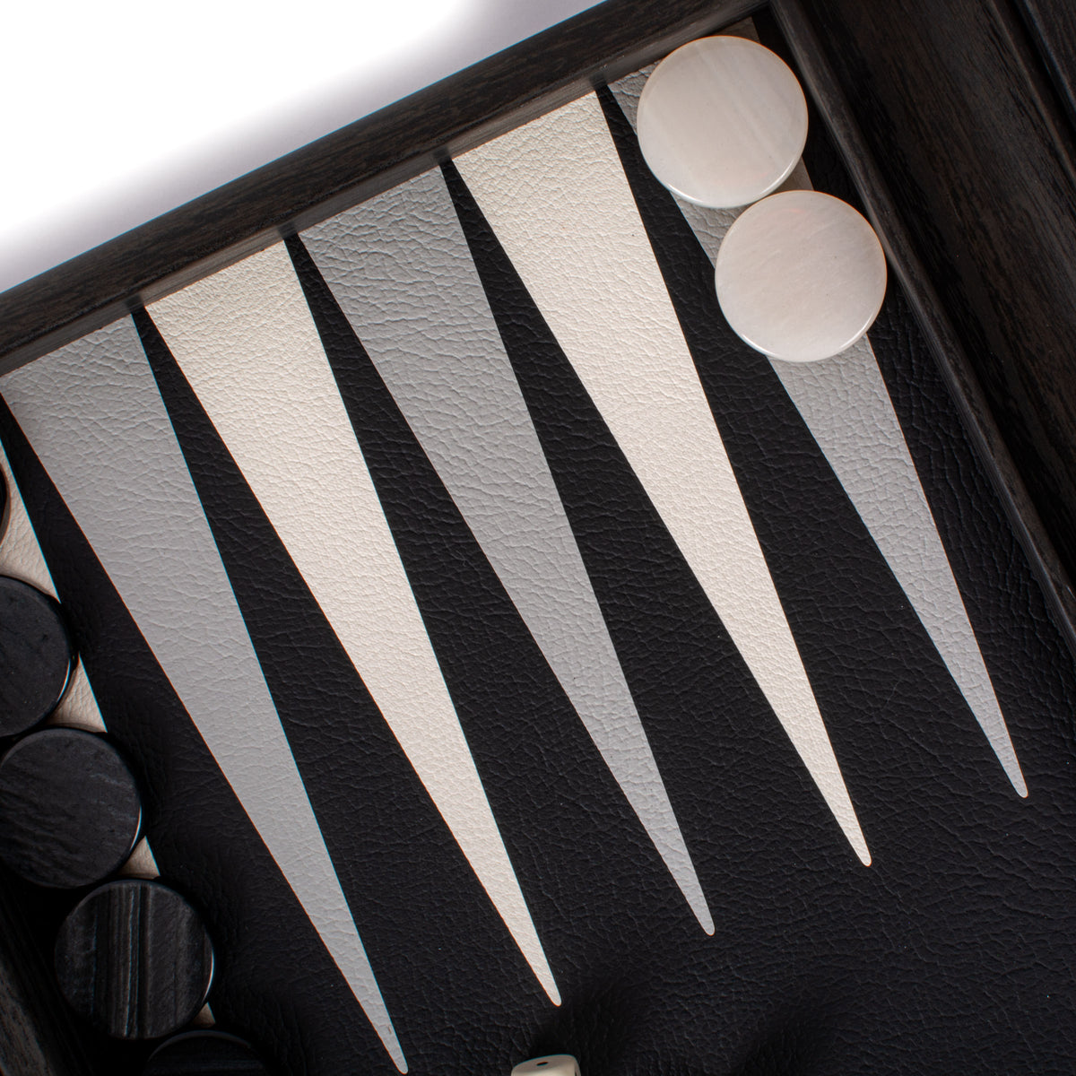 Close-up of a premium black leatherette backgammon board with cream and charcoal points and white and black playing pieces from MANOPOULOS