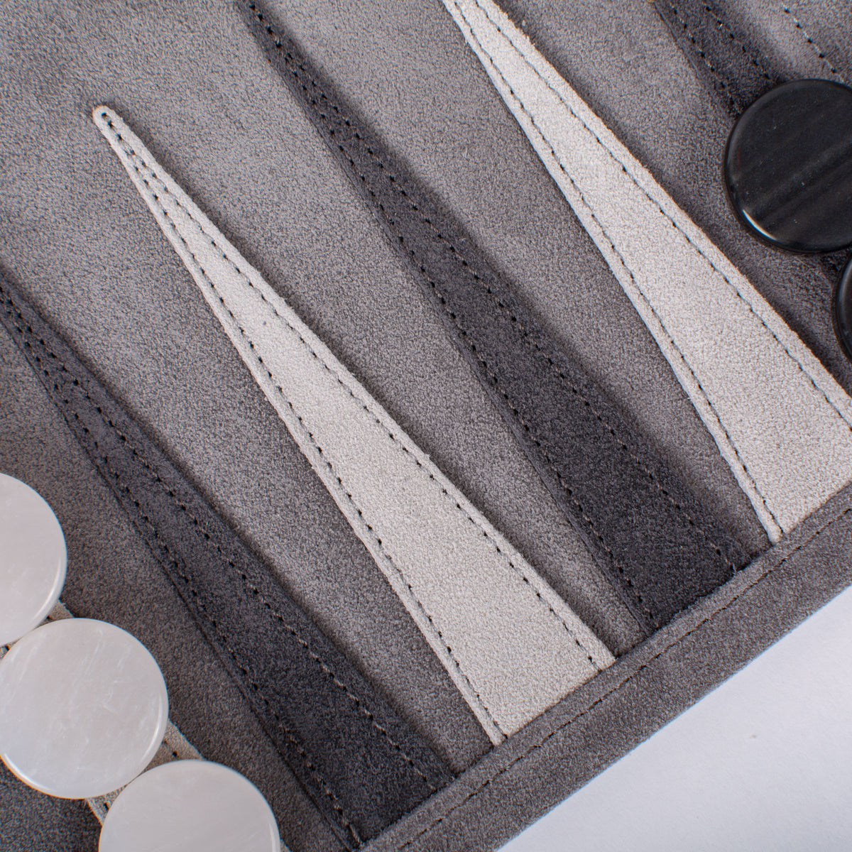 Close up of a grey suede roll up backgammon board with contrasting stitched leather strips and white and black playing pieces by Manopoulos Chess and Backgammon