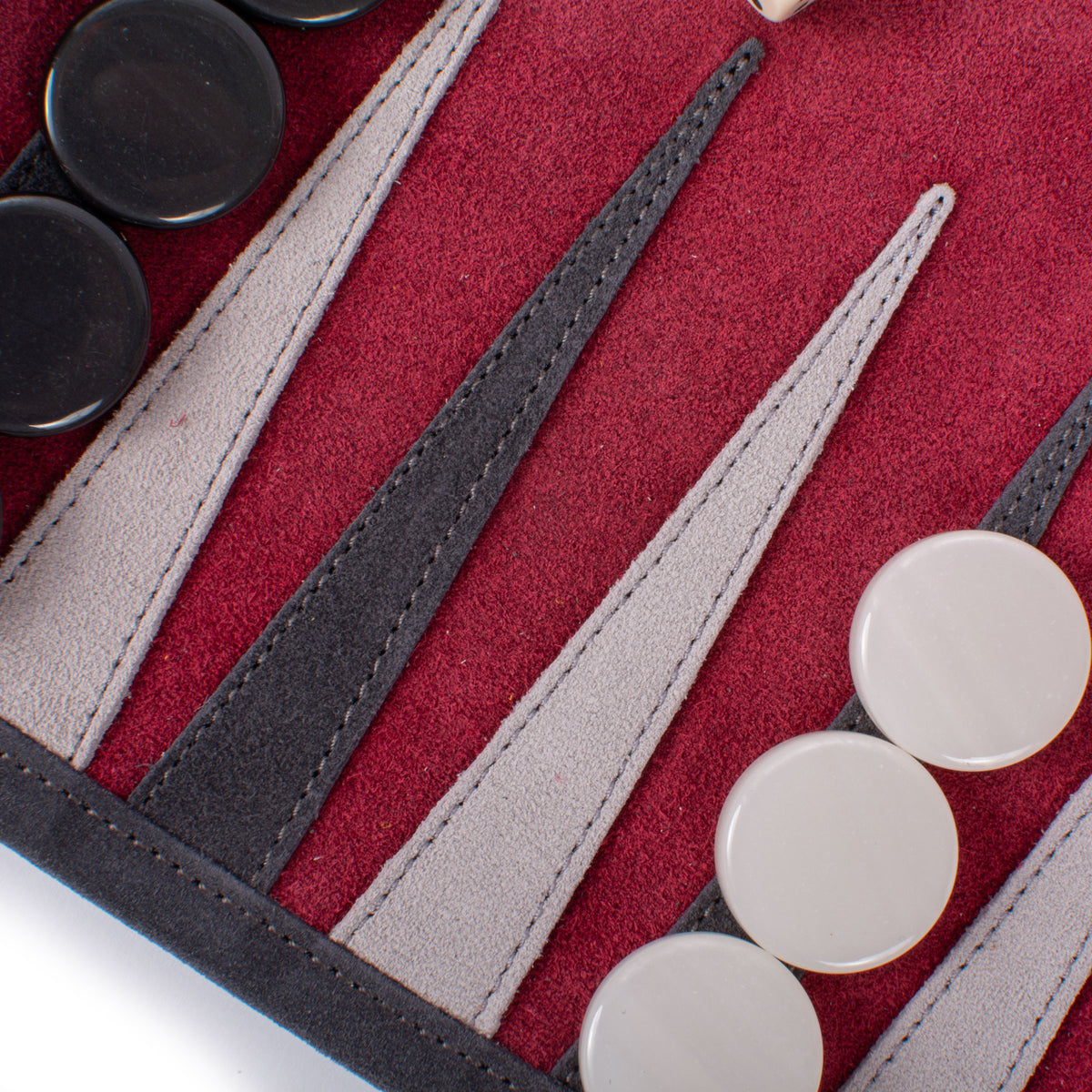 Close-up of a backgammon board with red felt, stitched black and cream leather points, and smooth black and ivory playing pieces.