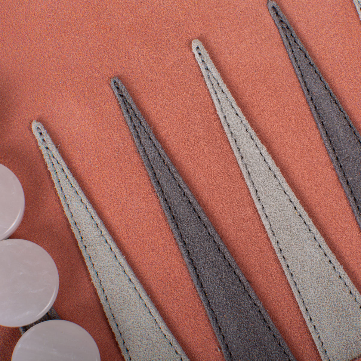 Close-up of a salmon suede backgammon board with alternating dark and light points and white checkers from MANOPOULOS Chess and Backgammon