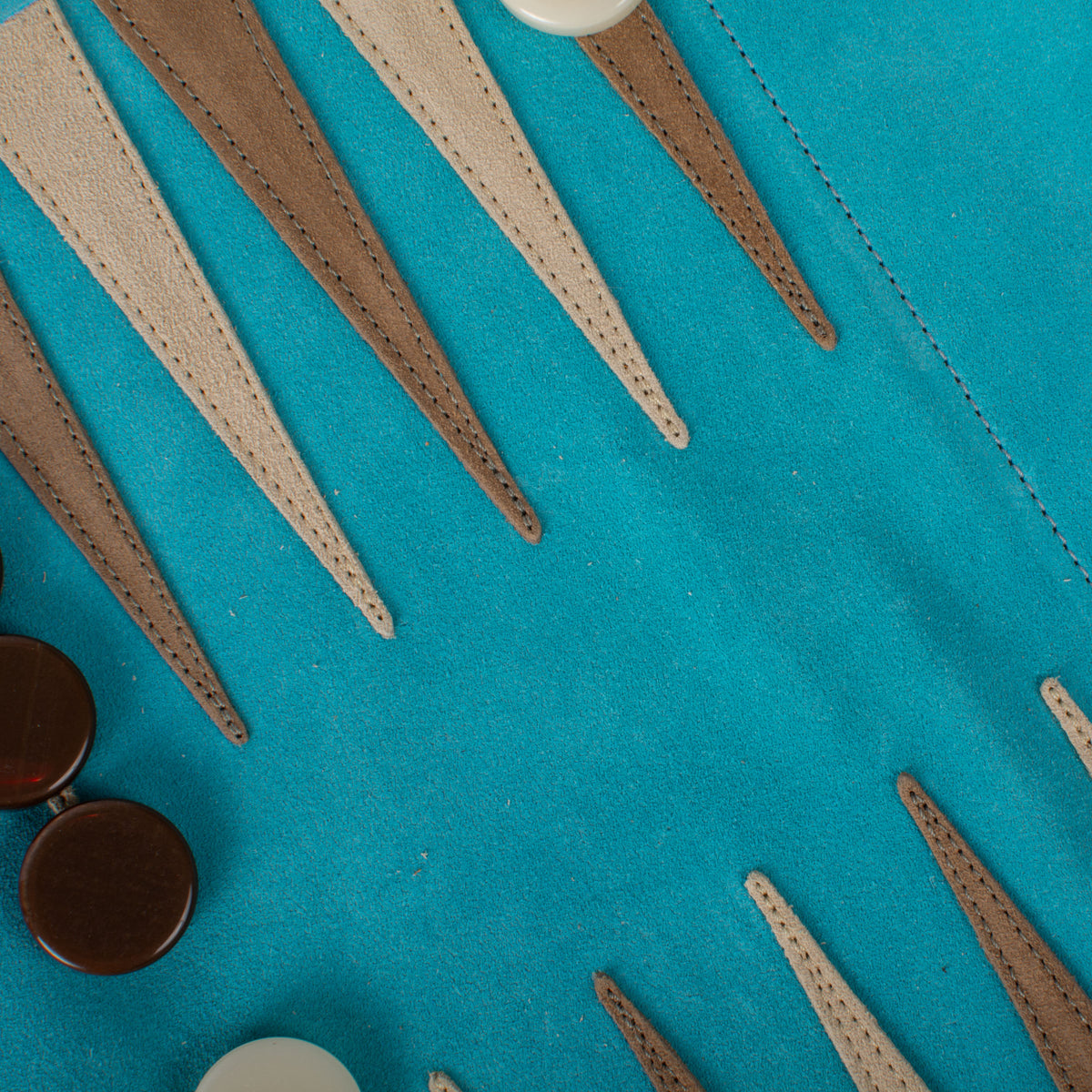 Close-up of a turquoise suede backgammon board with stitched tan and brown points and polished wooden checkers by Manopoulos Greek craftsmanship