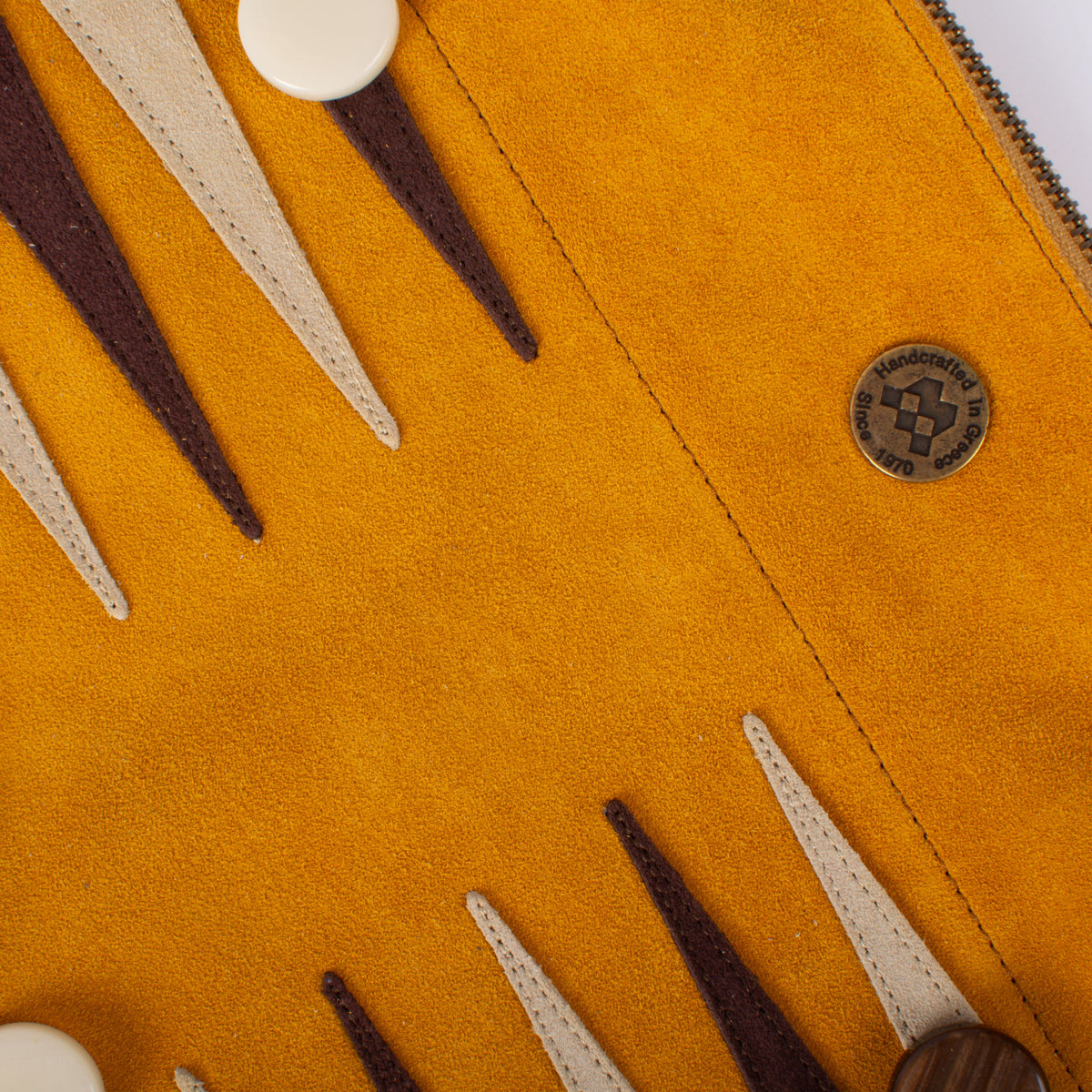 Close up of a warm yellow suede roll up backgammon set with brown and cream leather points and an artisan Manopoulos emblem from Greece