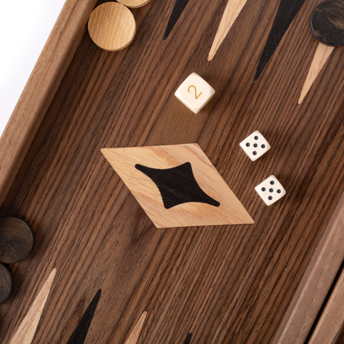 Close view of a dark wooden backgammon board with geometric inlay, round playing pieces, two dice, and a wooden tile marked with the number two