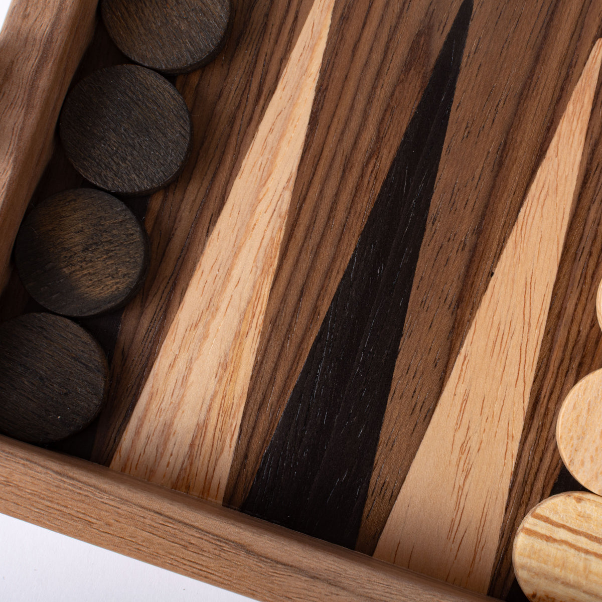 Close-up of a wooden backgammon board with striped grain and dark round playing pieces arranged along the edges