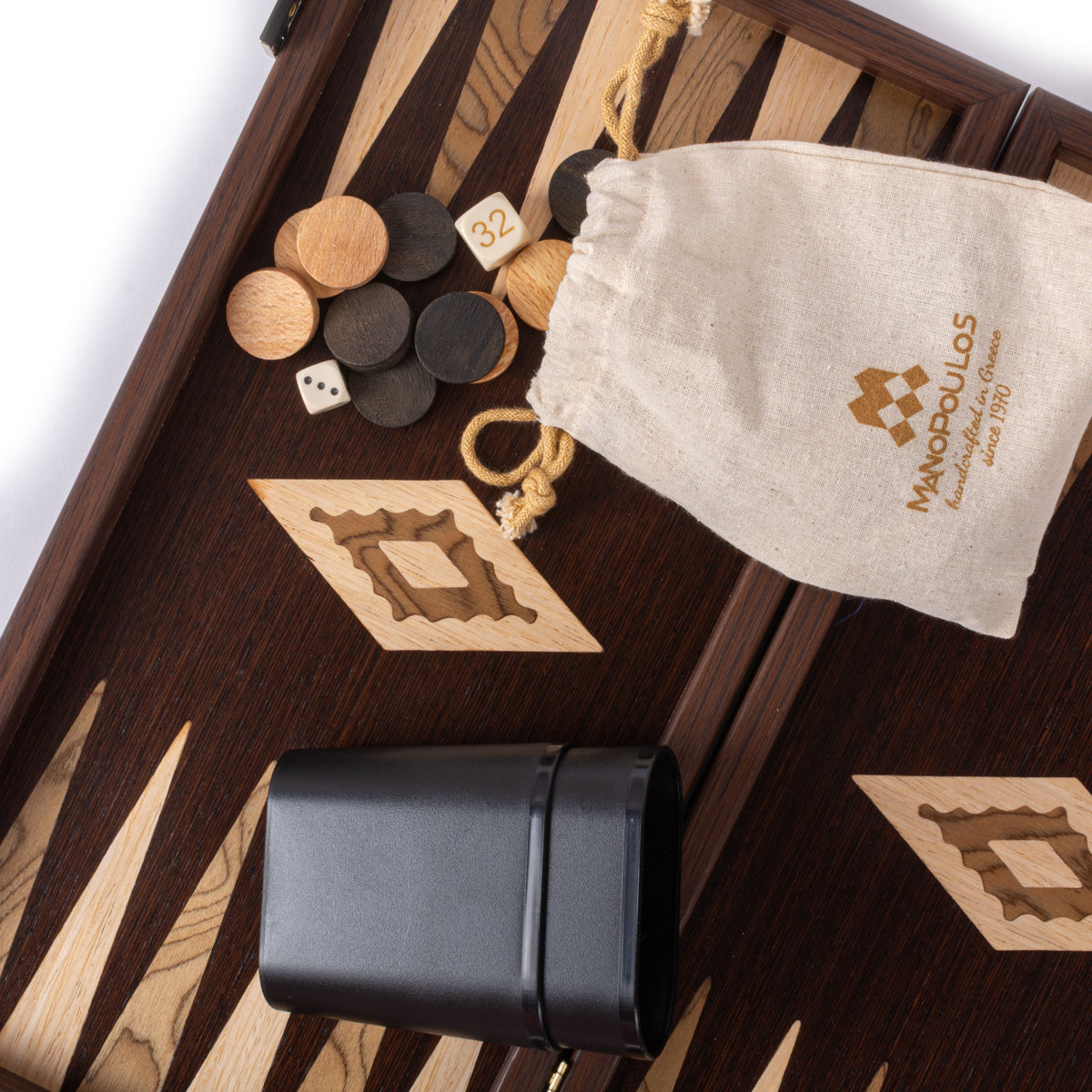 Close view of a handcrafted wenge and walnut burl backgammon board with marquetry inlay wooden checkers dice leather cup and MANOPOULOS Chess and Backgammon pouch